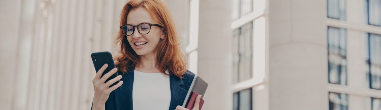 Happy european female holding mobile phone and smiling, reading good news from business partner